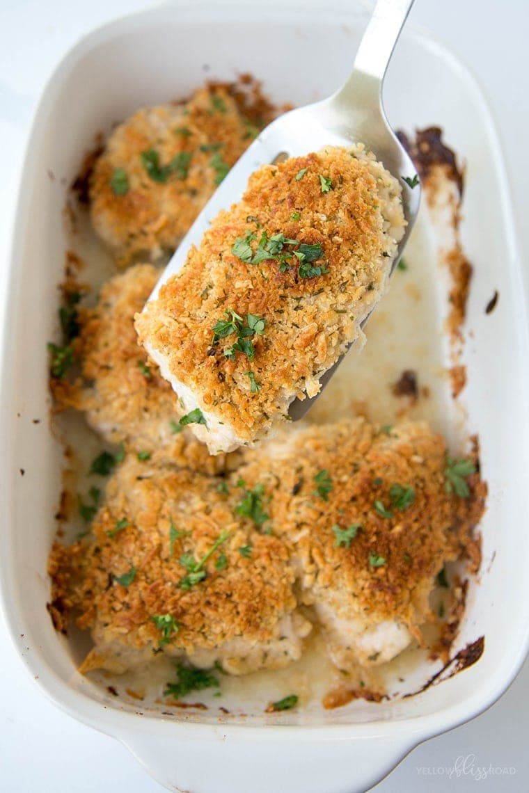 chicken breast pieces with crispy topping in a white dish. One piece held up with a spatula.