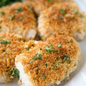 pieces of chicken breast with breading and minced parsley on a white plate.