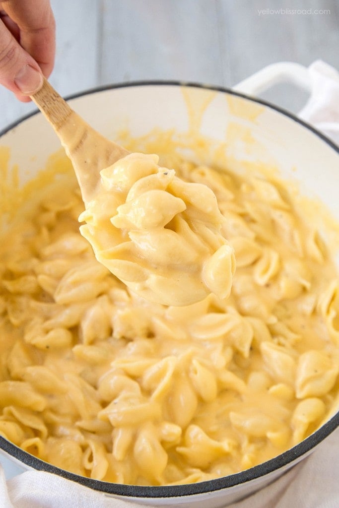 Shell pasta and cheese sauce in a white pot with a wooden spoon.