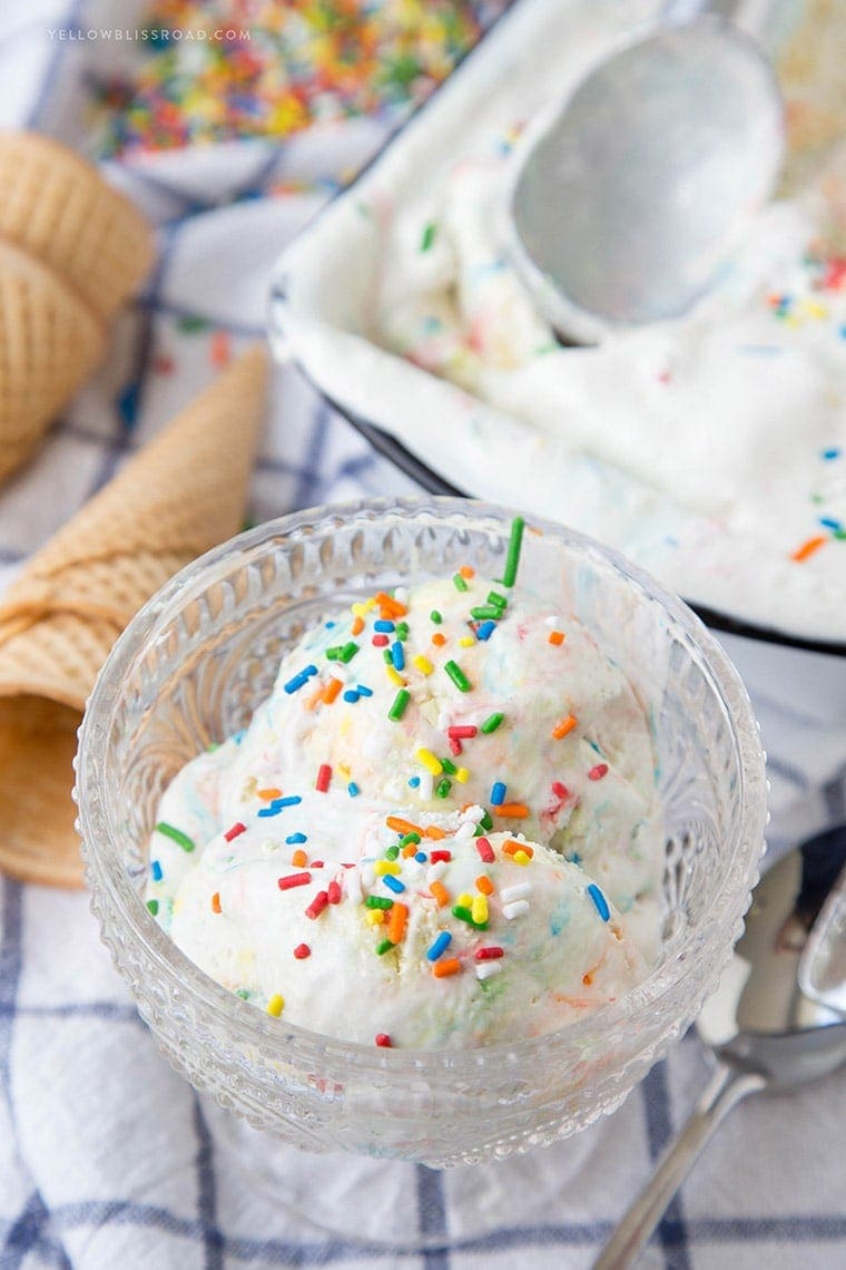 ice cream with sprinkles in a glass dish, ice cream cones, a blue and white napkin, a white loaf pan with ice cream