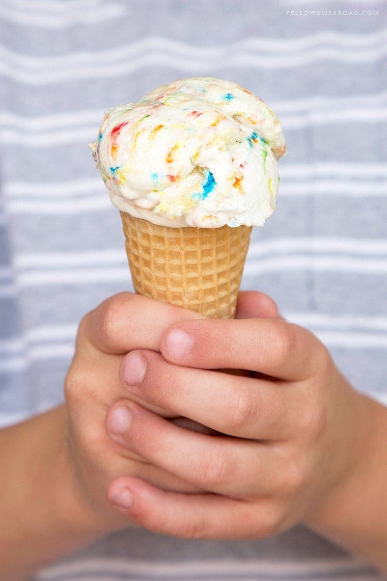 little hands holding an ice cream cone with ice cream and sprinkles.