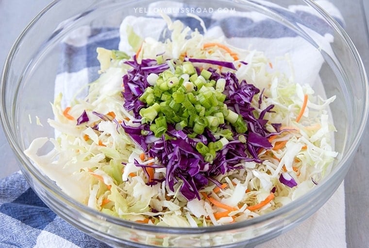 a glass bowl with coleslaw mix and green onions