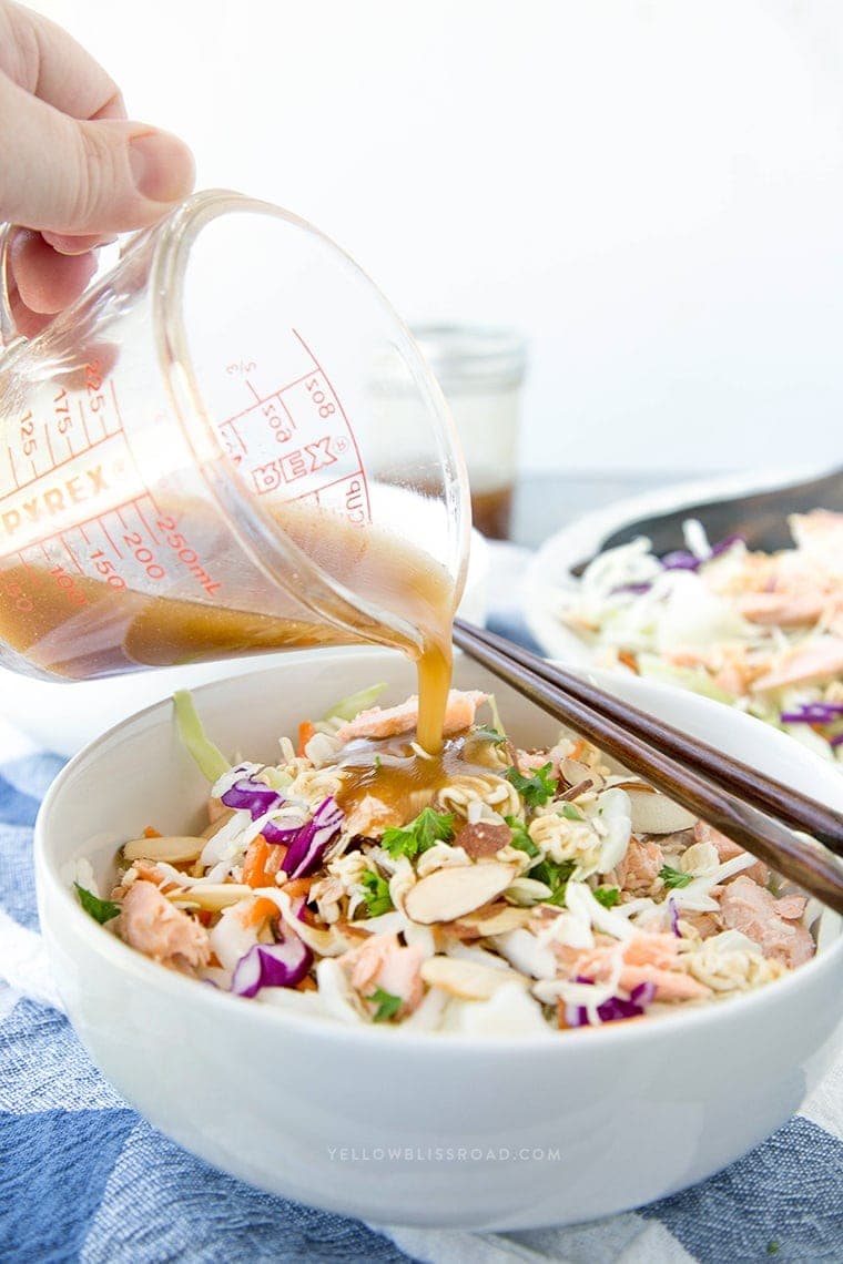 Asian dressing being poured over a bowl of ramen noodle salad