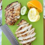 A cutting board with grilled chicken and citrus fruits