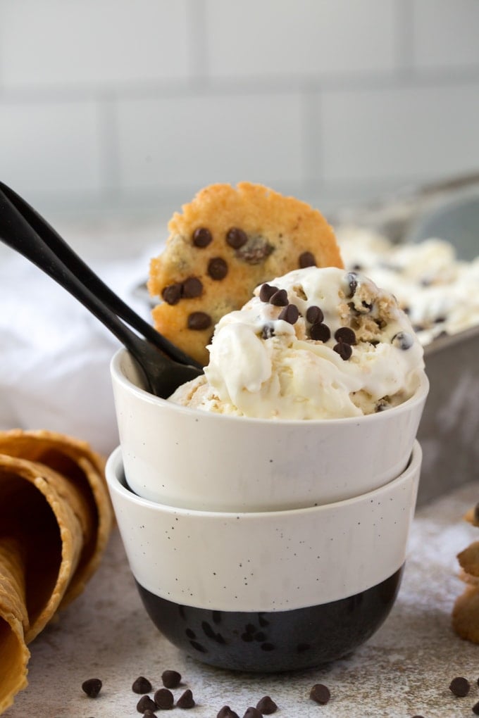 2 bowls stacked with cookie dough ice cream and a chocolate chip cookie on top with a black spoon.