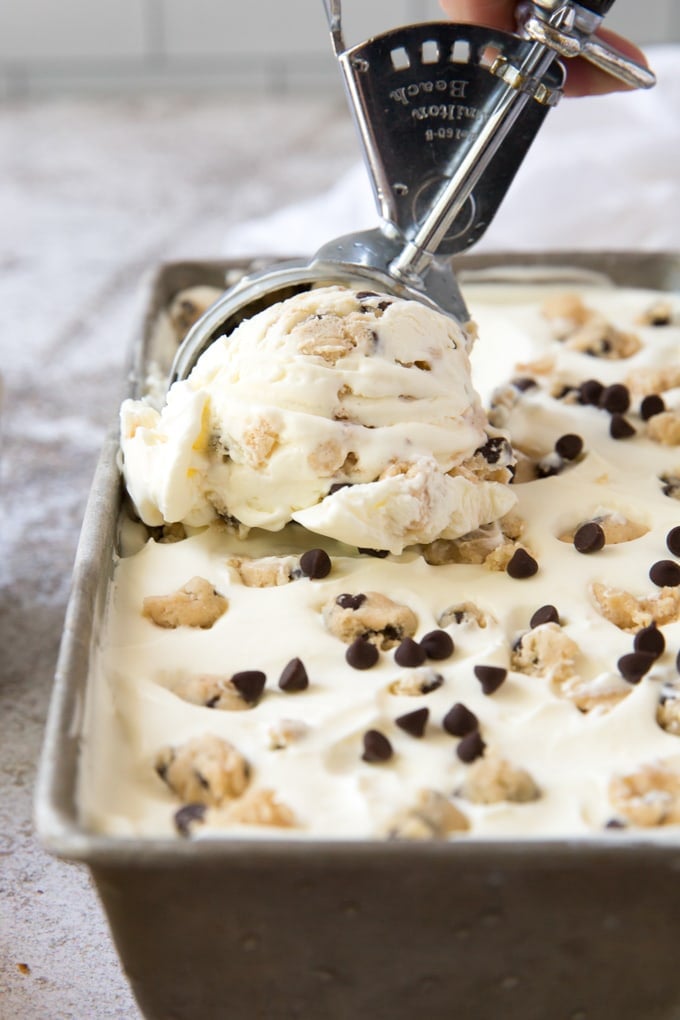 a silver loaf pan with cookie dough ice cream and chocolate chips with an ice cream scooper scooping a scoop of ice cream.