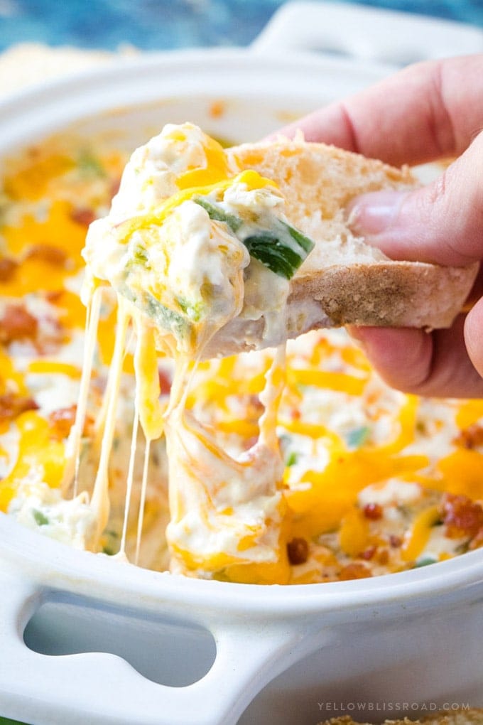 A hand holding a piece of bread lifting up a bite of jalapeno popper dip.