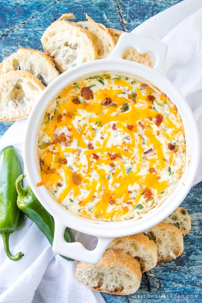 An overhead shot of jalapeno dip in a white bowl surrounded by slices of bread