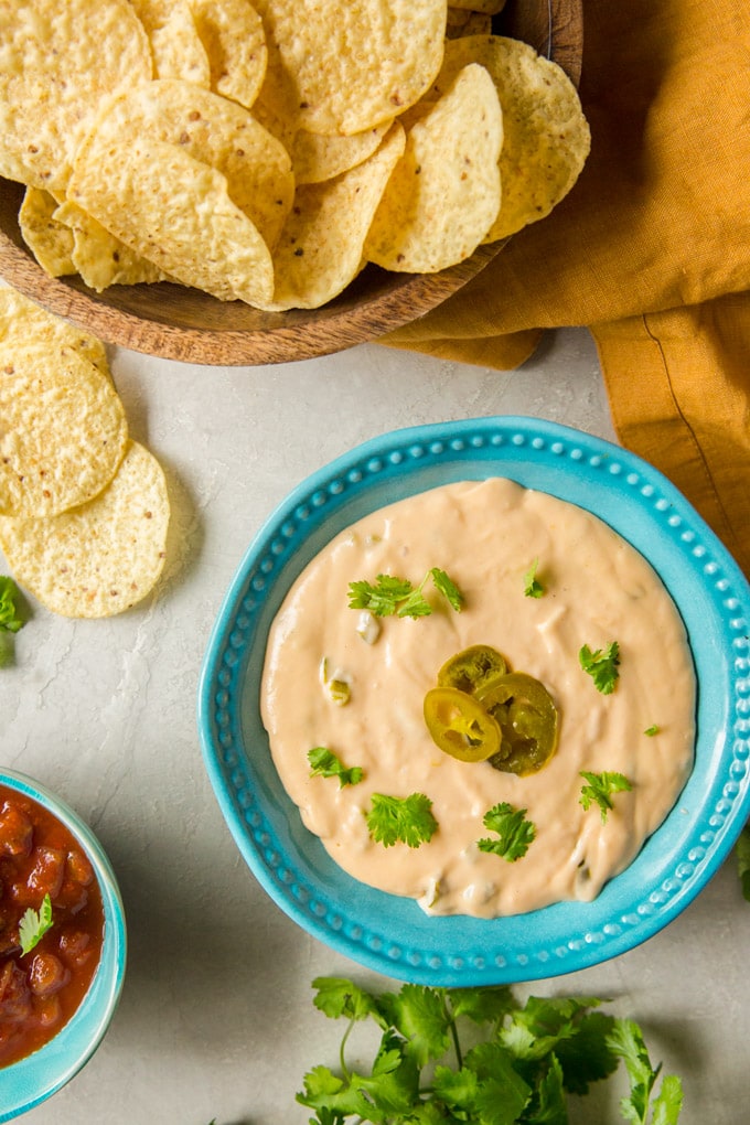 Nacho Cheese Sauce in a blue bowl surrounded by tortilla chips and salsa.