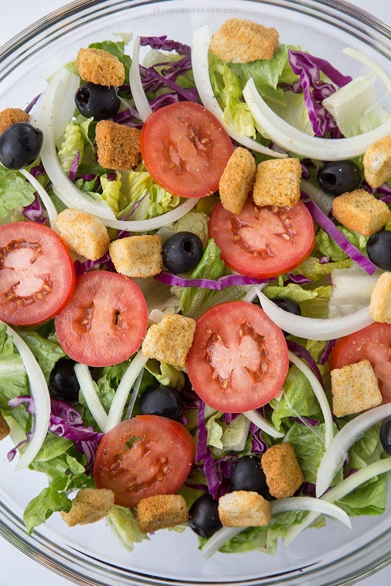 Overhead shot os lettuce, tomatoes, onions and olives in a bowl