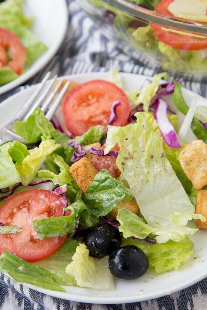 A close up of a salad with tomatoes, olive, onions and croutons