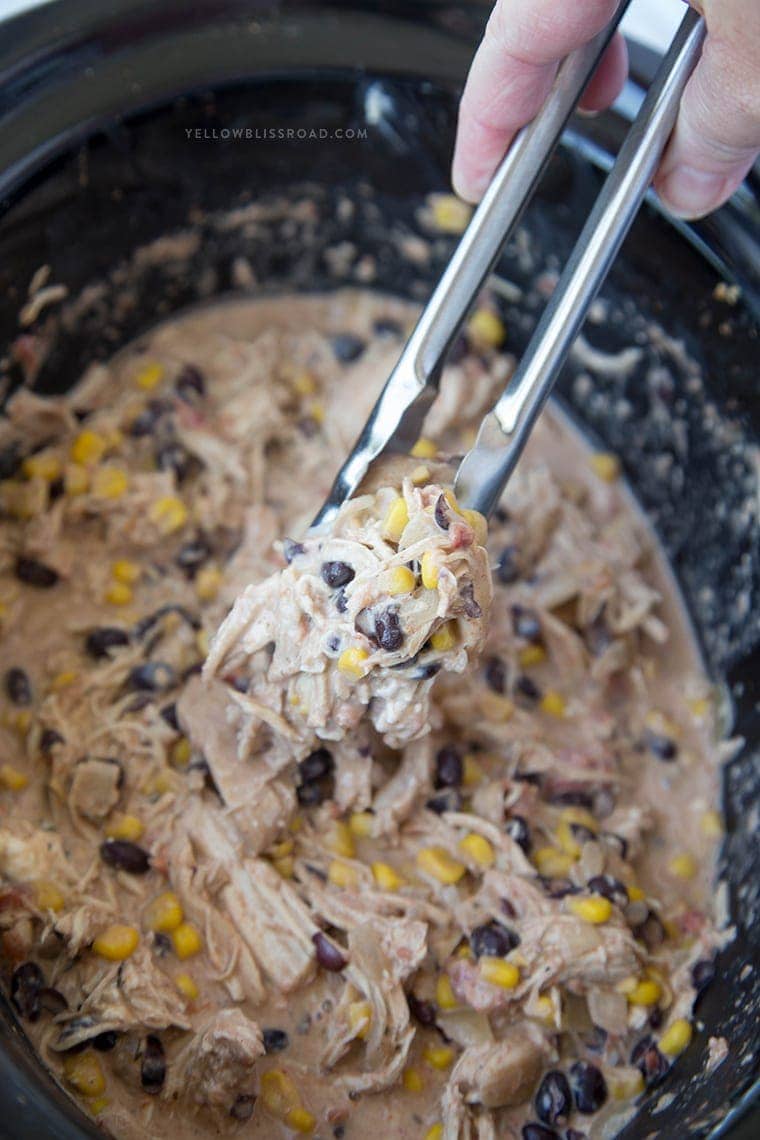 Tongs lifting creamy taco ranch chicken in a slow cooker
