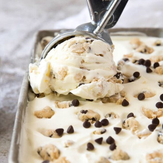 a square image of cookie dough ice cream being scooped with a metal ice cream scooper out of a metal container.
