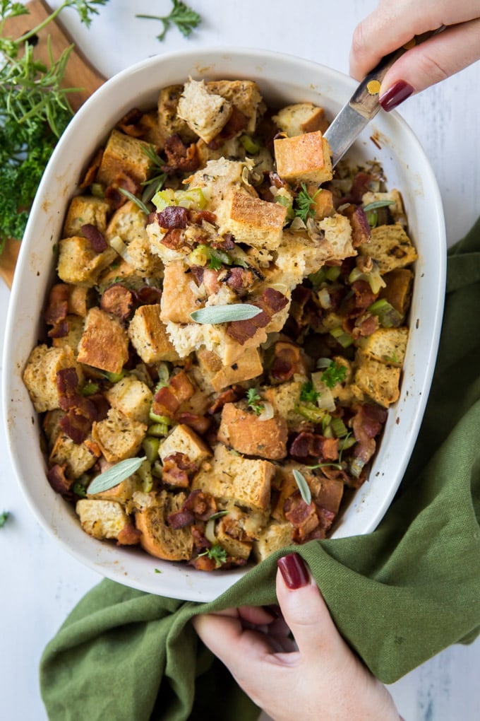 A dish of stuffing with a hand and spoon scooping out a serving