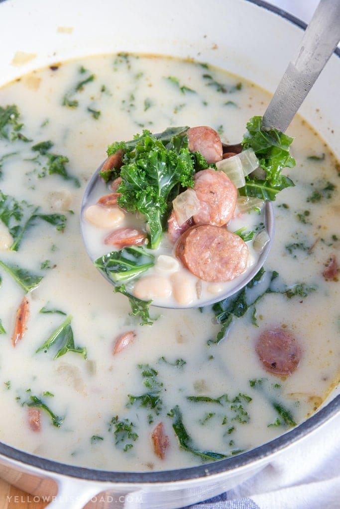 A ladle full of sausage, kale and beans in a creamy broth