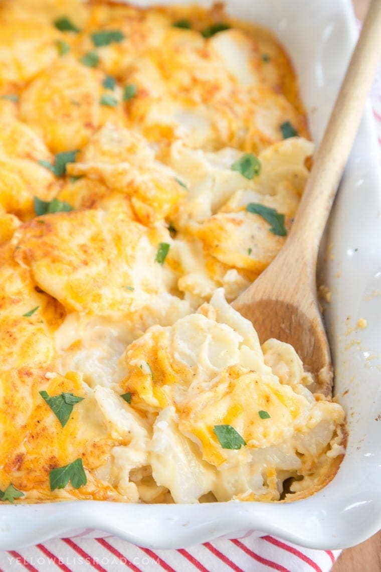 Cheesy Scalloped Potatoes in a large casserole dish with a wooden spoon
