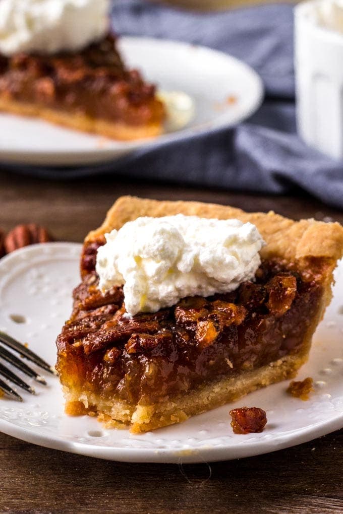 This classic Pecan Pie Recipe is filled with crunchy pecans baked with a sweet filling. This beautiful pie will steal the show on your dessert table. A slice of pecan pie topped with whipped cream.