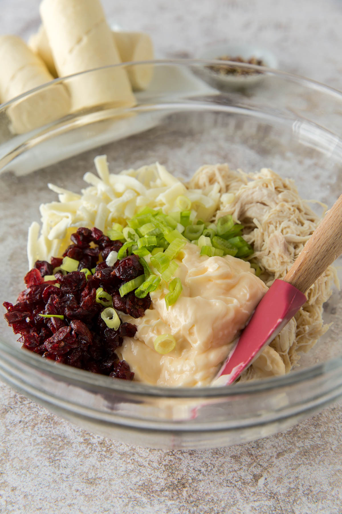 glass bowl, spatula, shredded chicken, mayo, cranberries, cheese, green onion, crescent roll dough