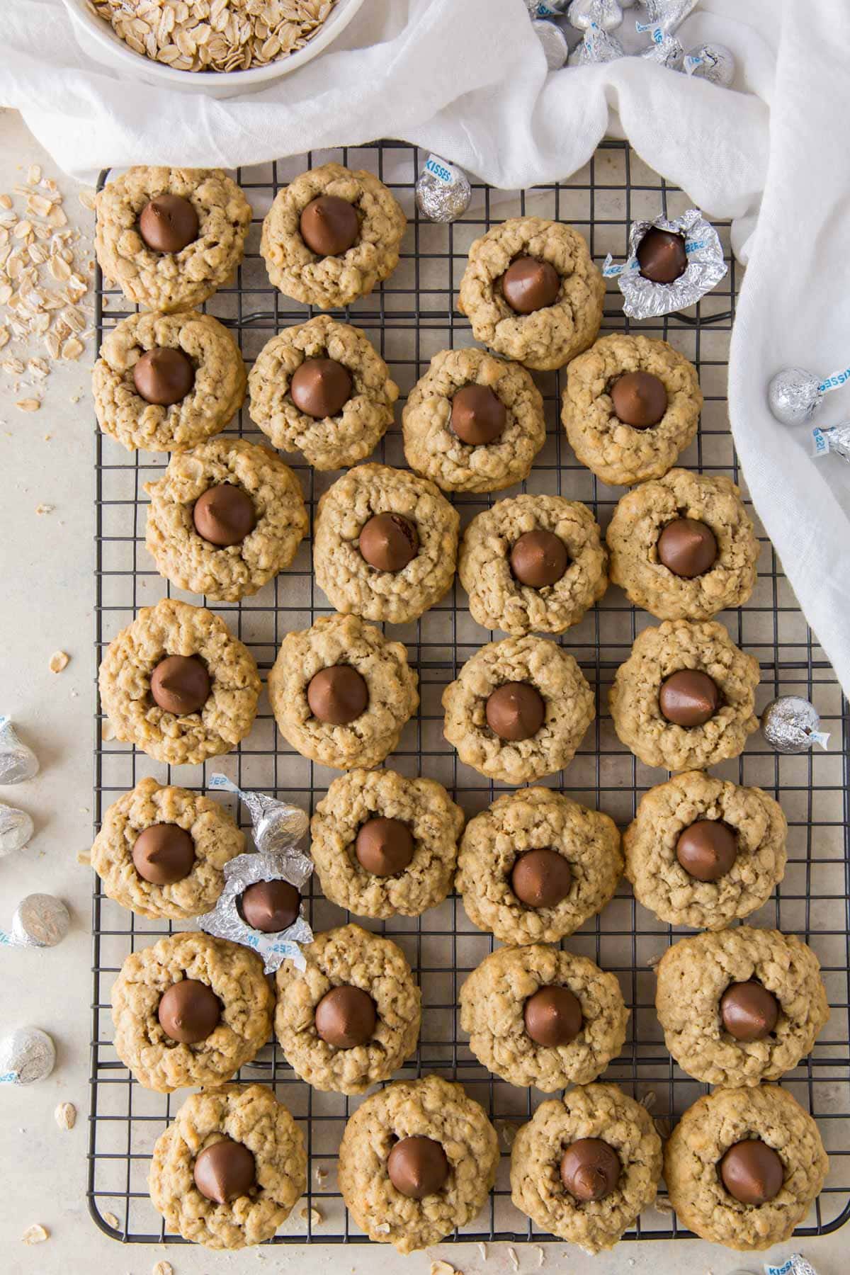 oatmeal kiss cookies on a wire rack, white towel, oats in a white bowl, hershey kisses