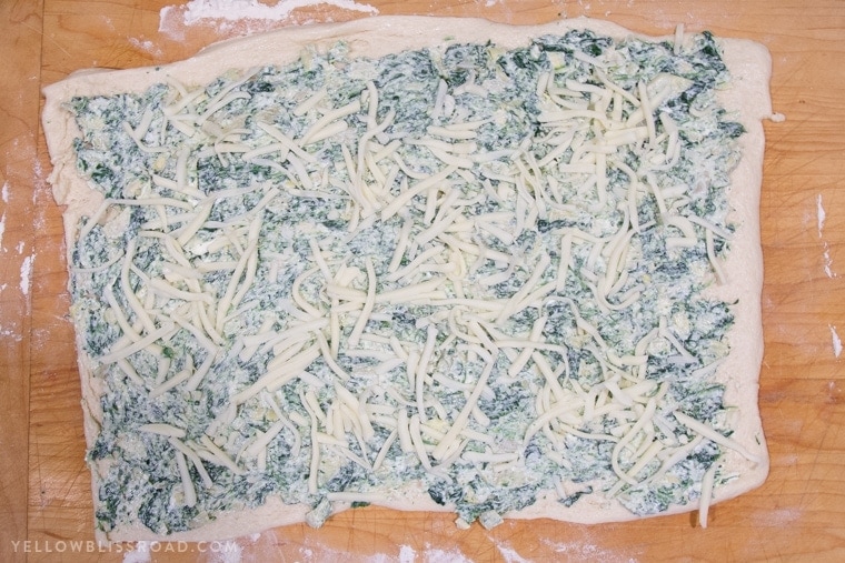Creamy delicious Spinach Artichoke Dip spread out on pizza dough and topped with mozzarella cheese.