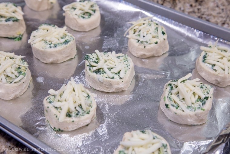 Creamy delicious Spinach Artichoke Dip Pinwheels on a cookie sheet before baking.