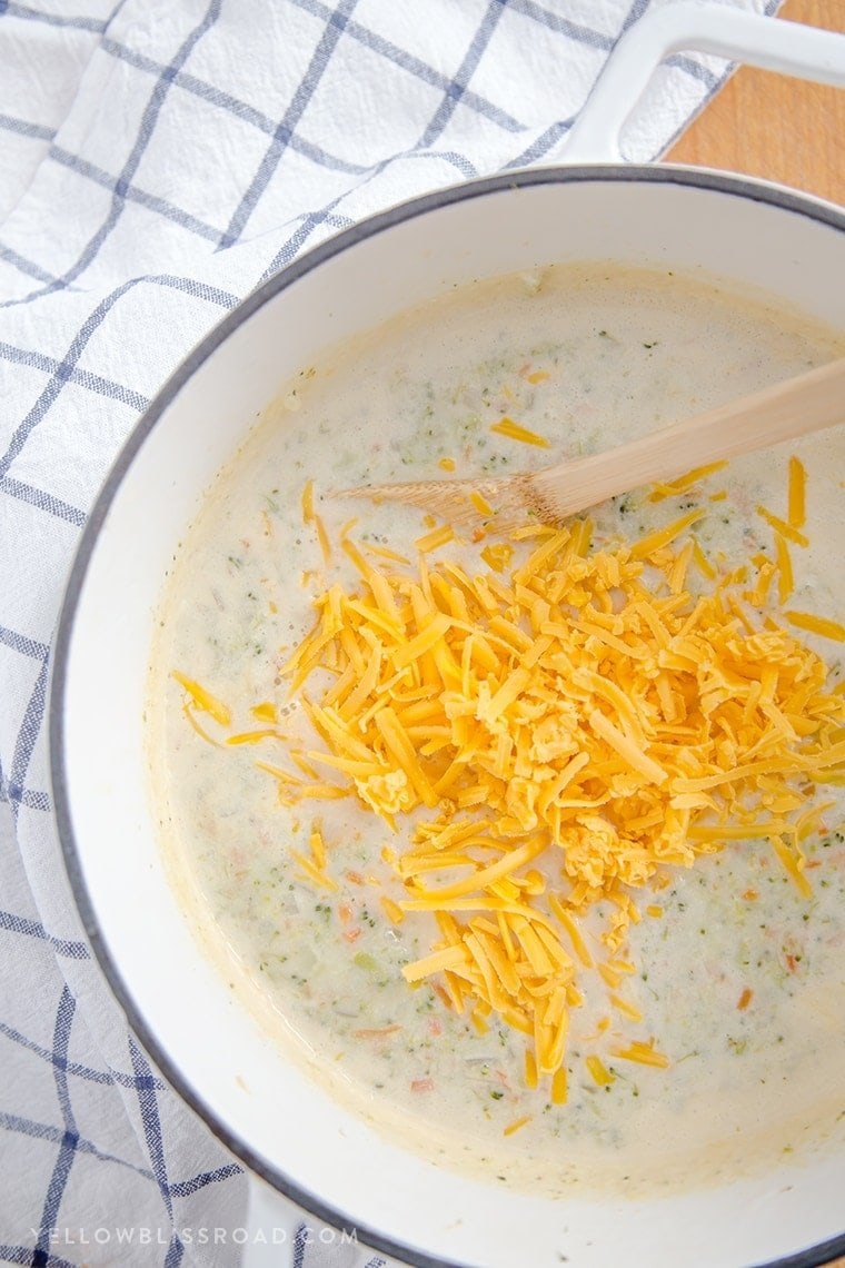 a large pot of broccoli cheese soup with shredded cheddar cheese