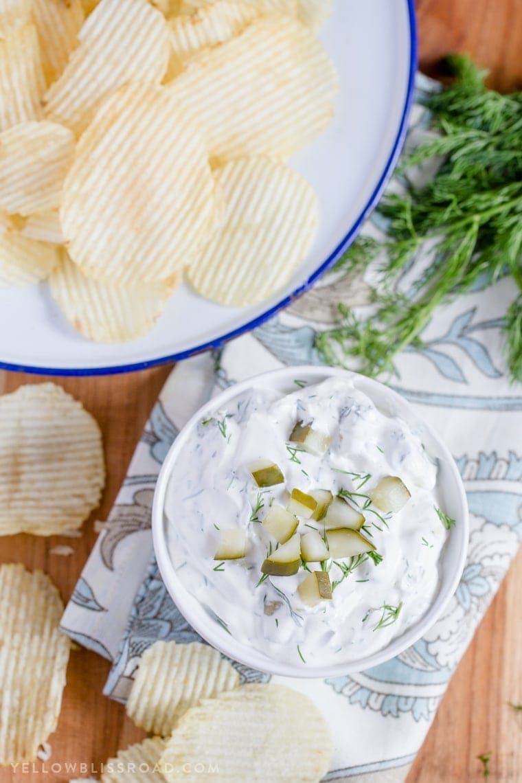 Dill pickle dip in a small bowl and a larger bowl of potato chips.