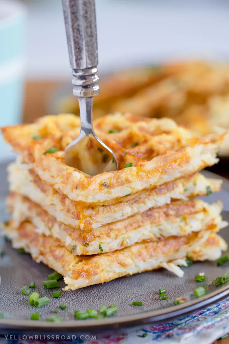 A stack of fresh, crispy Egg & Cheese Hash Brown Waffles with a fork in them.