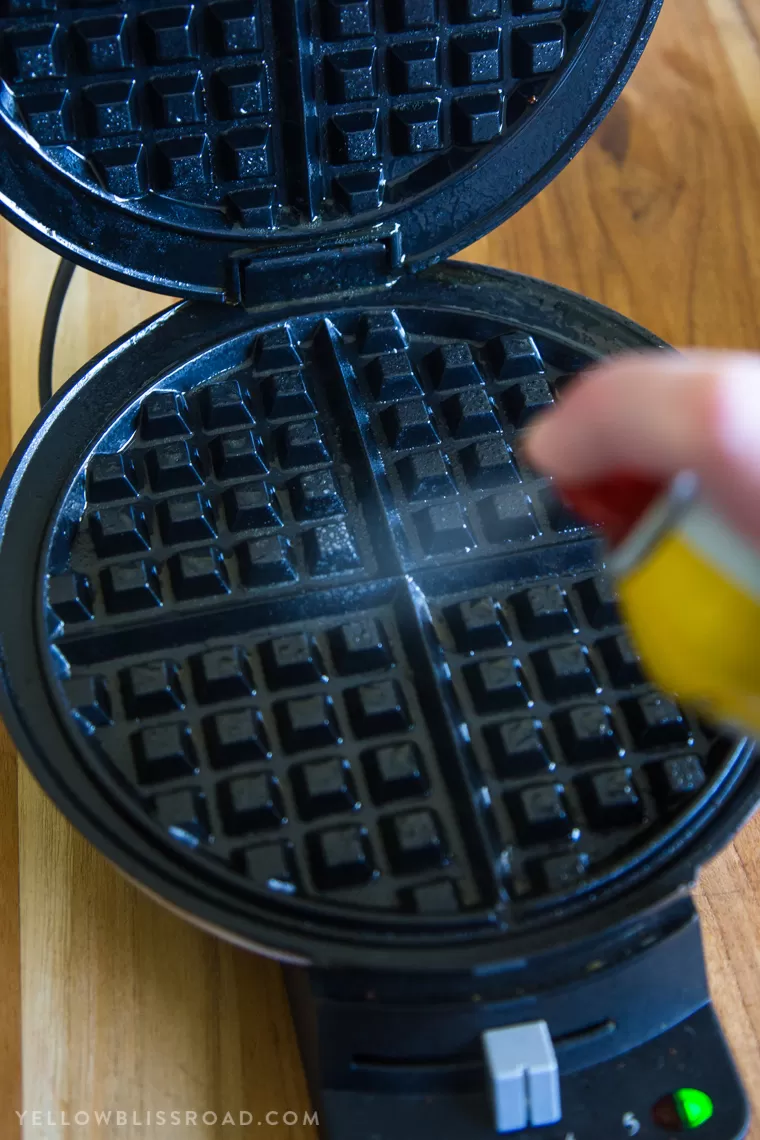 Spraying a waffle maker with nonstick cooking spray for Egg & Cheese Hash Brown Waffles