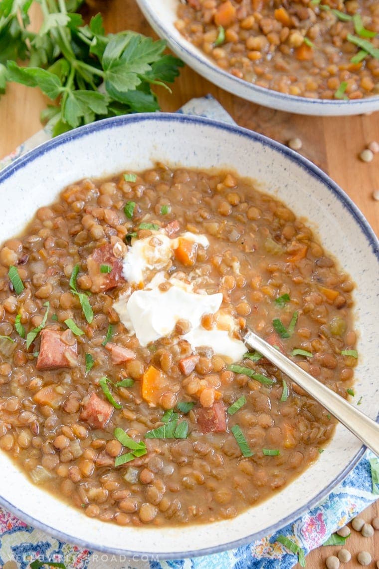 white bowl with a blue rim, filled with lentils and ham, sour cream and a spoon, parsley and a colorful napkin