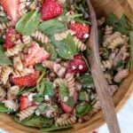 A bowl of pasta salad with strawberries and spinach