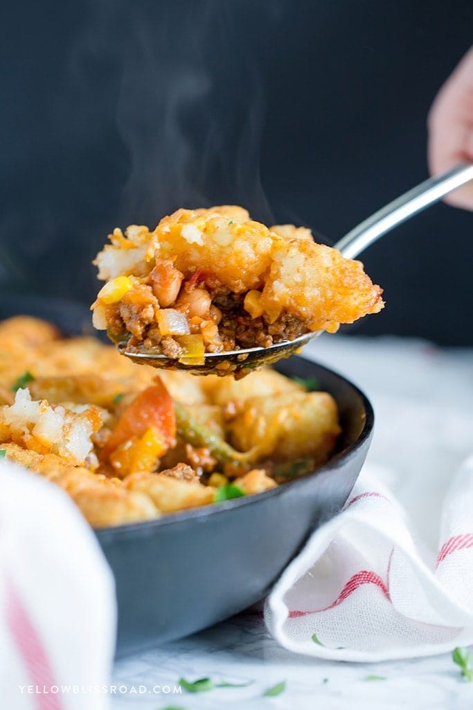 A scoop of tater tot casserole with beef and veggies on a silver spoon