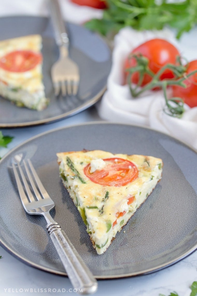 A slice of a tomato and asparagus frittata on a gray plate.