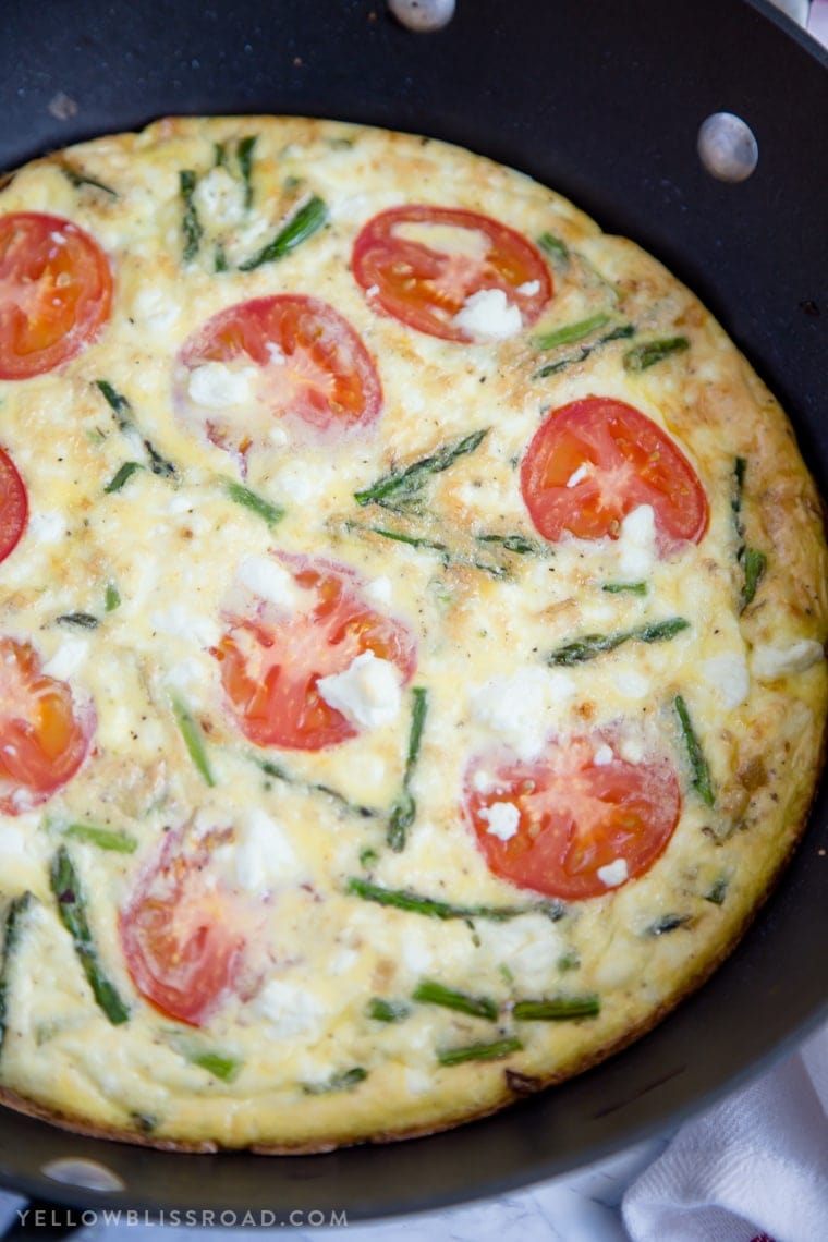 A frittata with goat cheese, asparagus and tomatoes in a skillet.