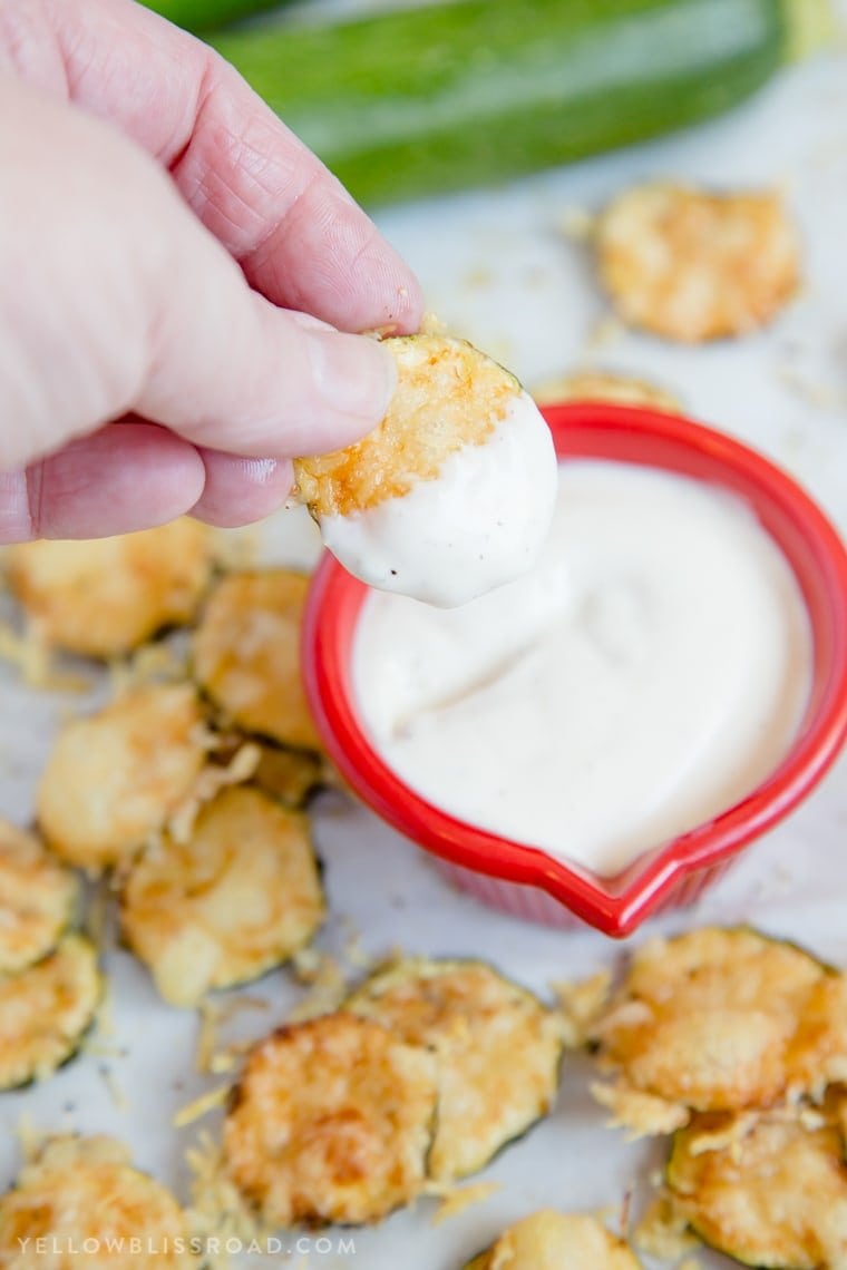 Baked Parmesan Zucchini Crisps are a highly addictive snack that is simple to make with just two ingredients! You'll love these healthy zucchini chips! a zucchini chip dipped in ranch dressing
