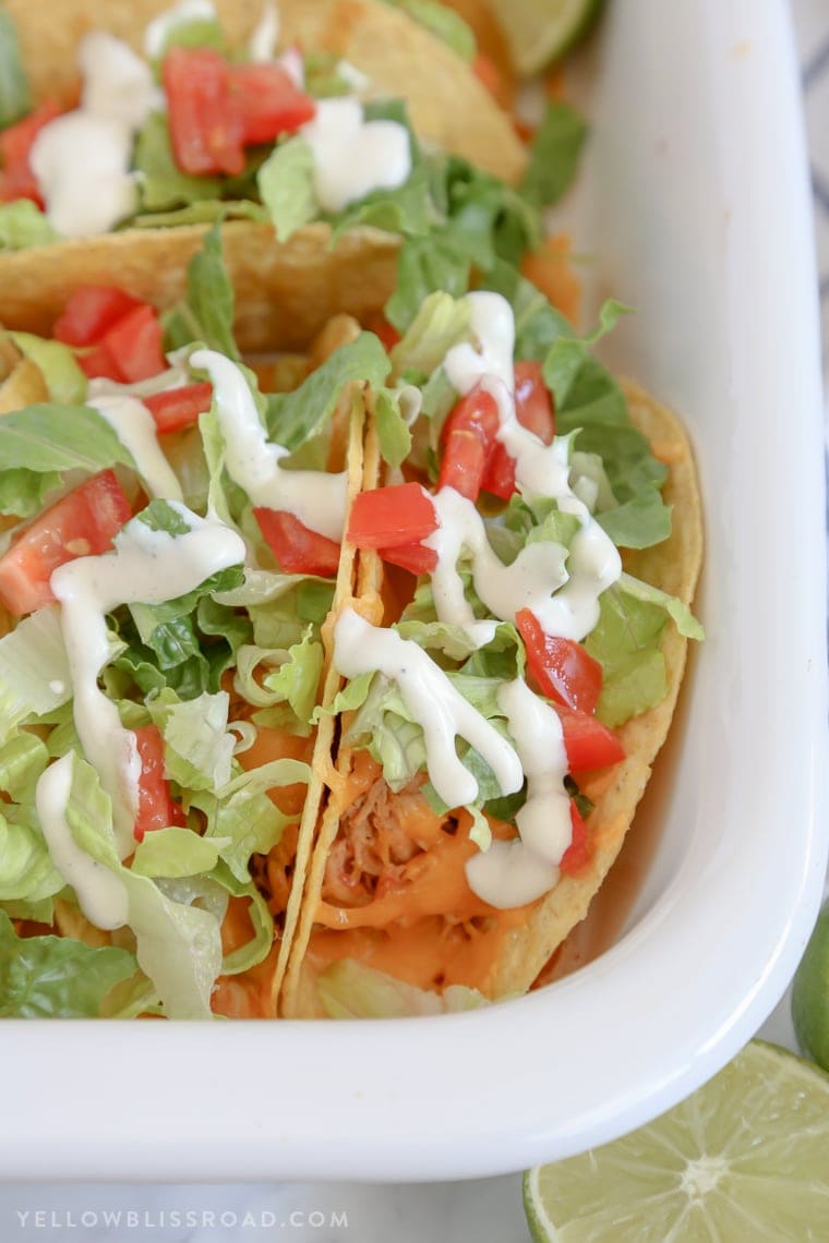 Tacos with chicken, lettuce and tomatoes and ranch dressing drizzle in a white dish