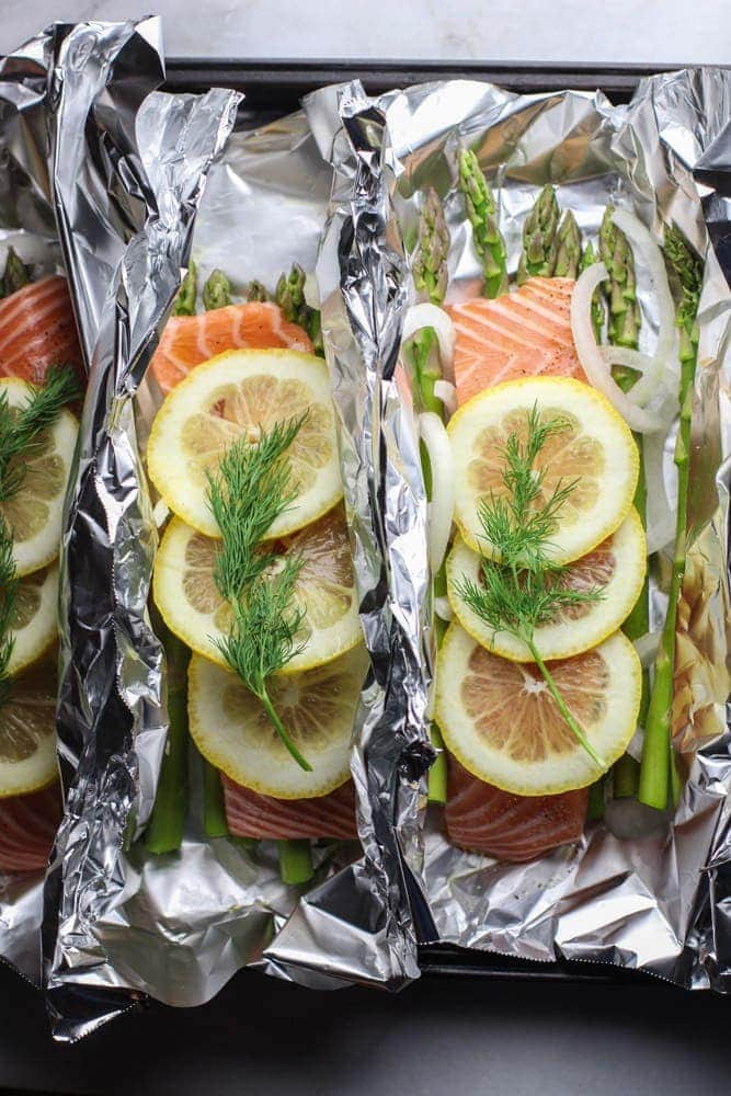 foil with pieces of salmon, lemon slices, dill and asparagus.
