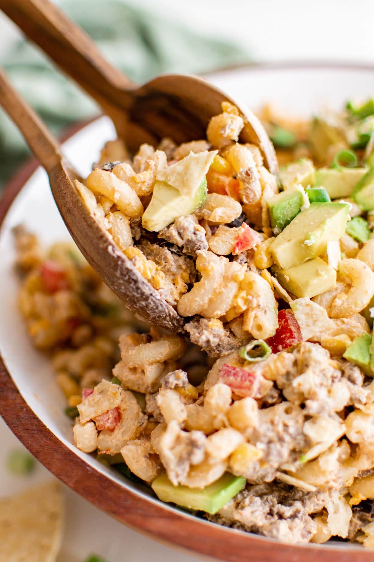 Salad tongs lifting a portion of taco pasta salad from a large bowl.