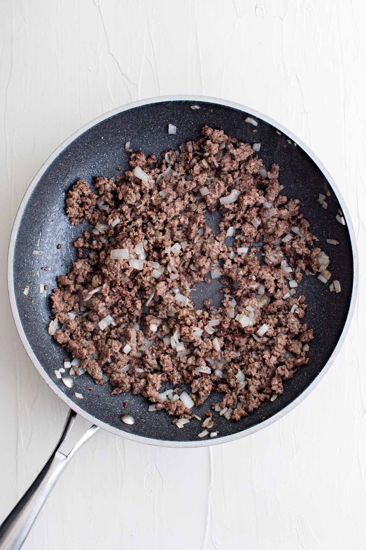 Cooked ground beef and onions in a skillet.