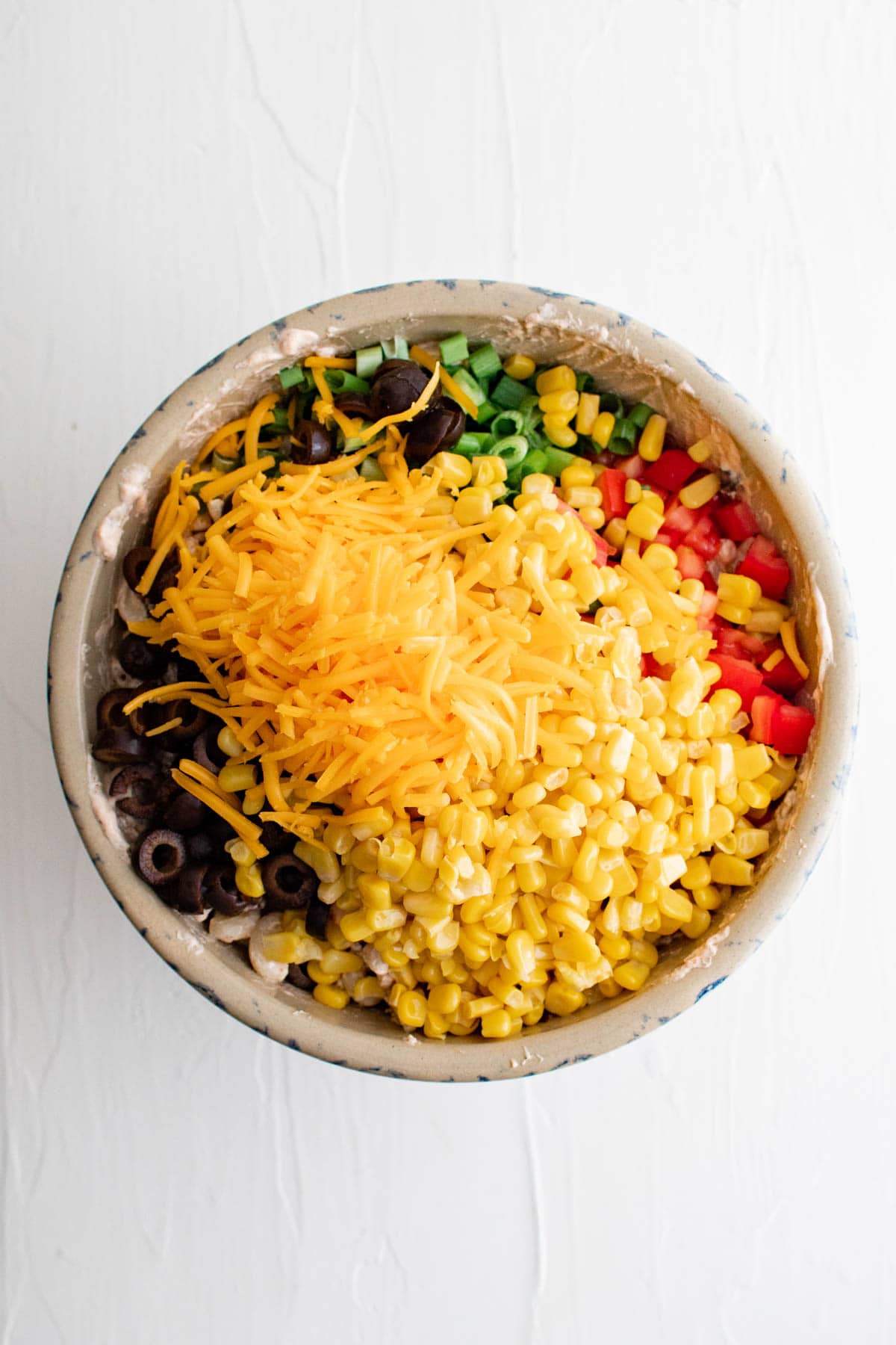Olives, tomatoes, green onions, corn and shredded cheese in a large bowl.