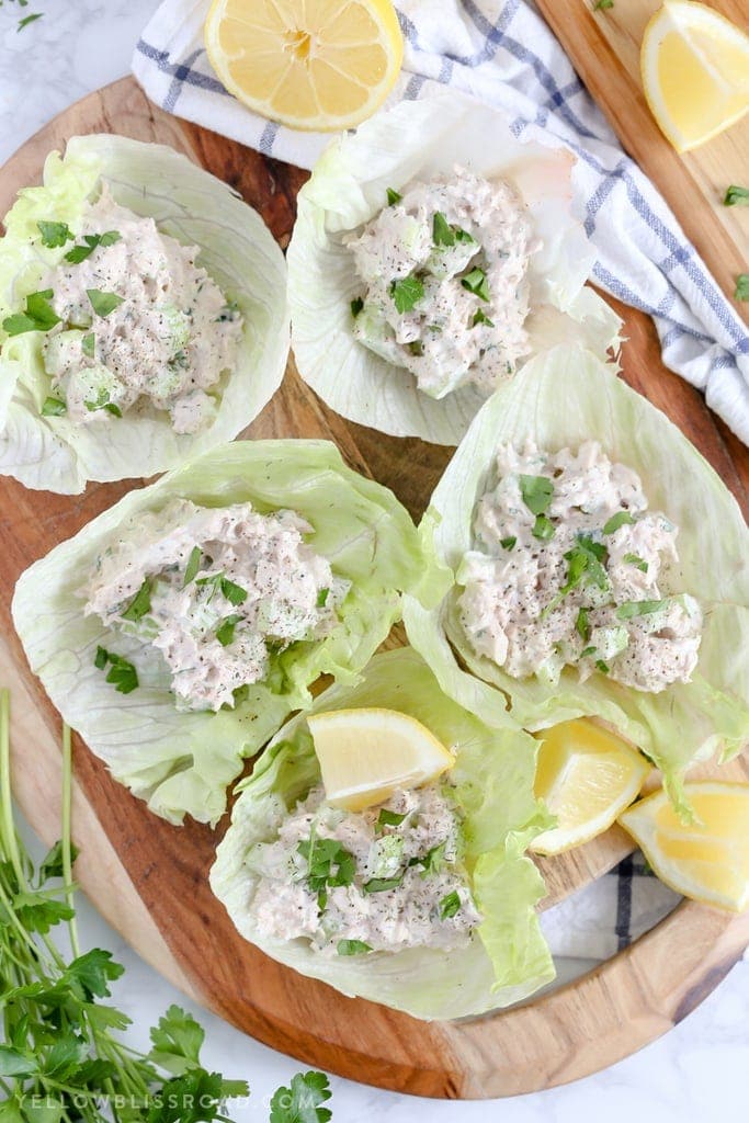 5 iceberg lettuce cups with tuna salad, lemon wedges and parsley on a wood background
