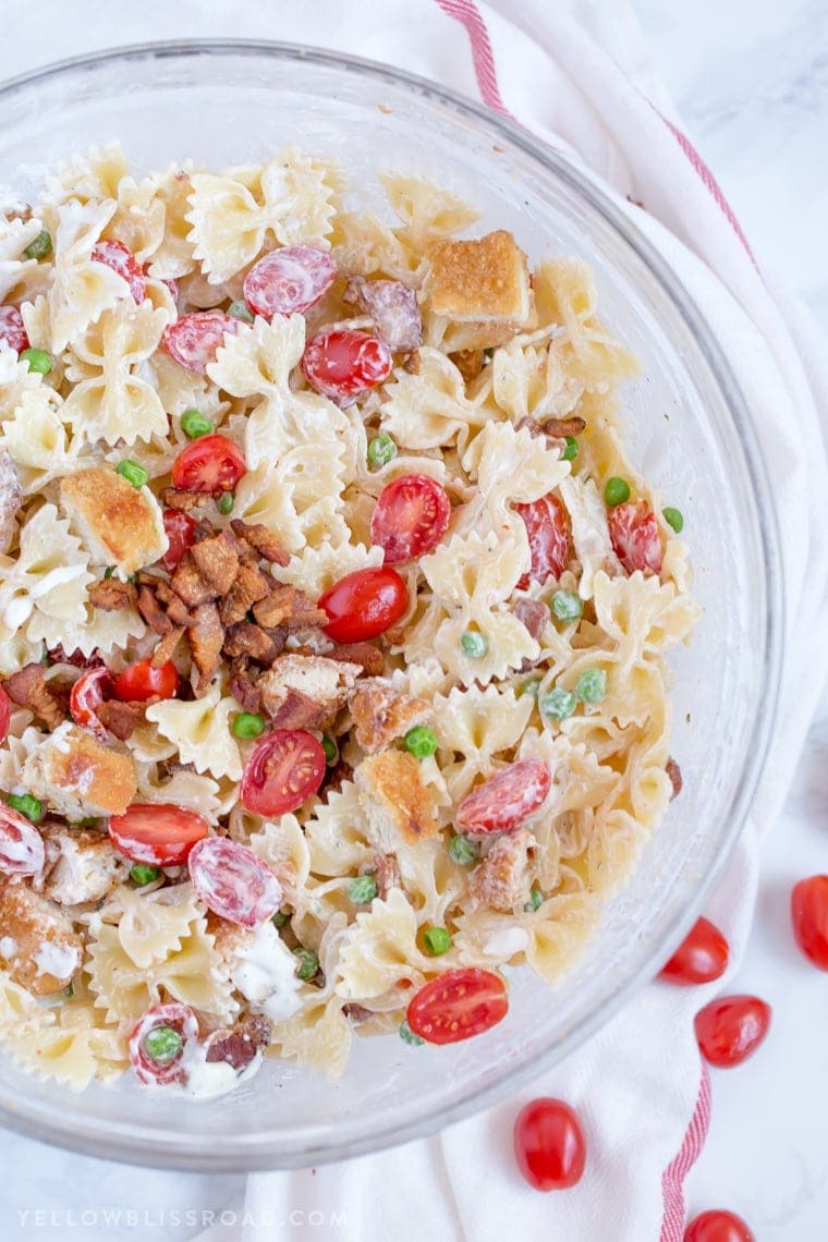 bacon, chicken, tomatoes, pasta and peas in a large glass bowl. a few scattered tomatoes and a red and white napkin