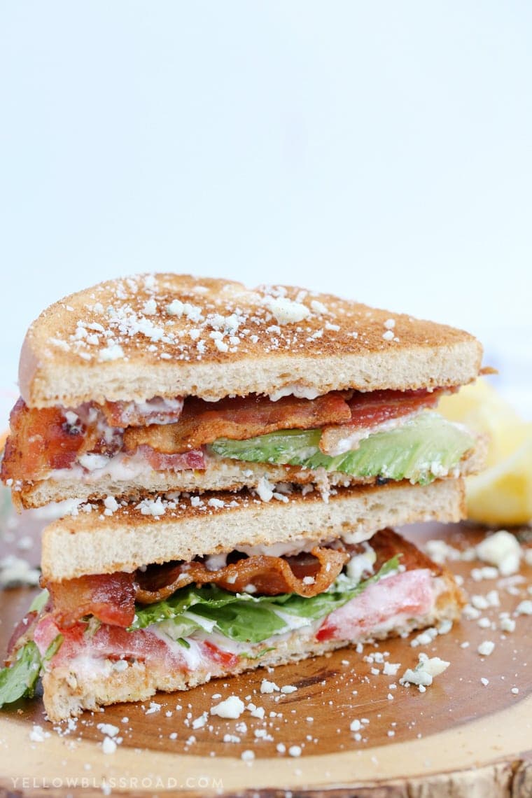 two halves of a blt sandwich stacked on top of each other with blue cheese sprinkles around the wood cutting board