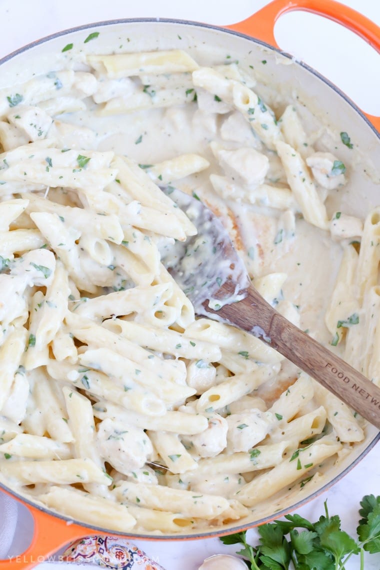 A skillet full of Creamy Garlic Penne Pasta with Chicken with a wooden spoon.