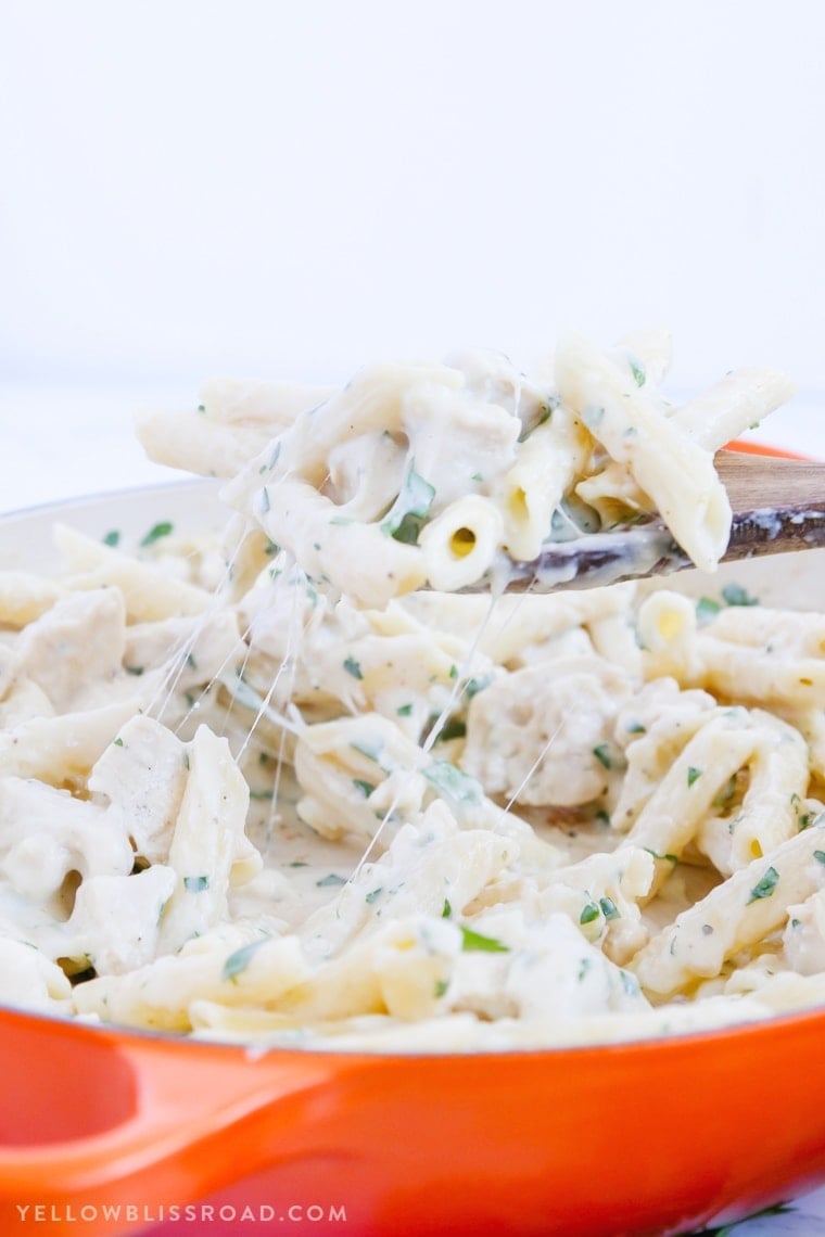 Creamy Garlic Penne Pasta on a wooden spoon being lifted out of a skillet.