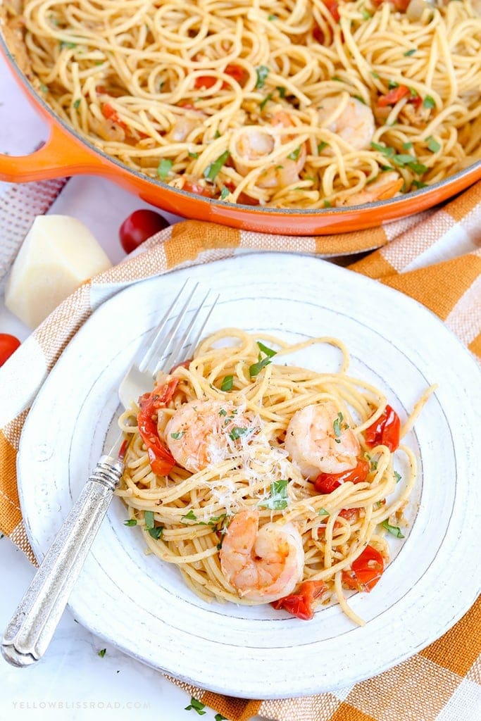 a white plate with pasta and shrimp, an orange skillet with pasta and shrimp. An orange and white napkin.