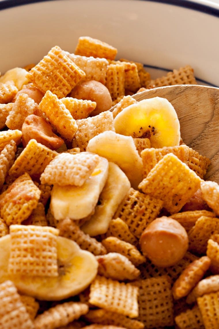 A close up of a bowl of tropical chex mix with a wooden spoon