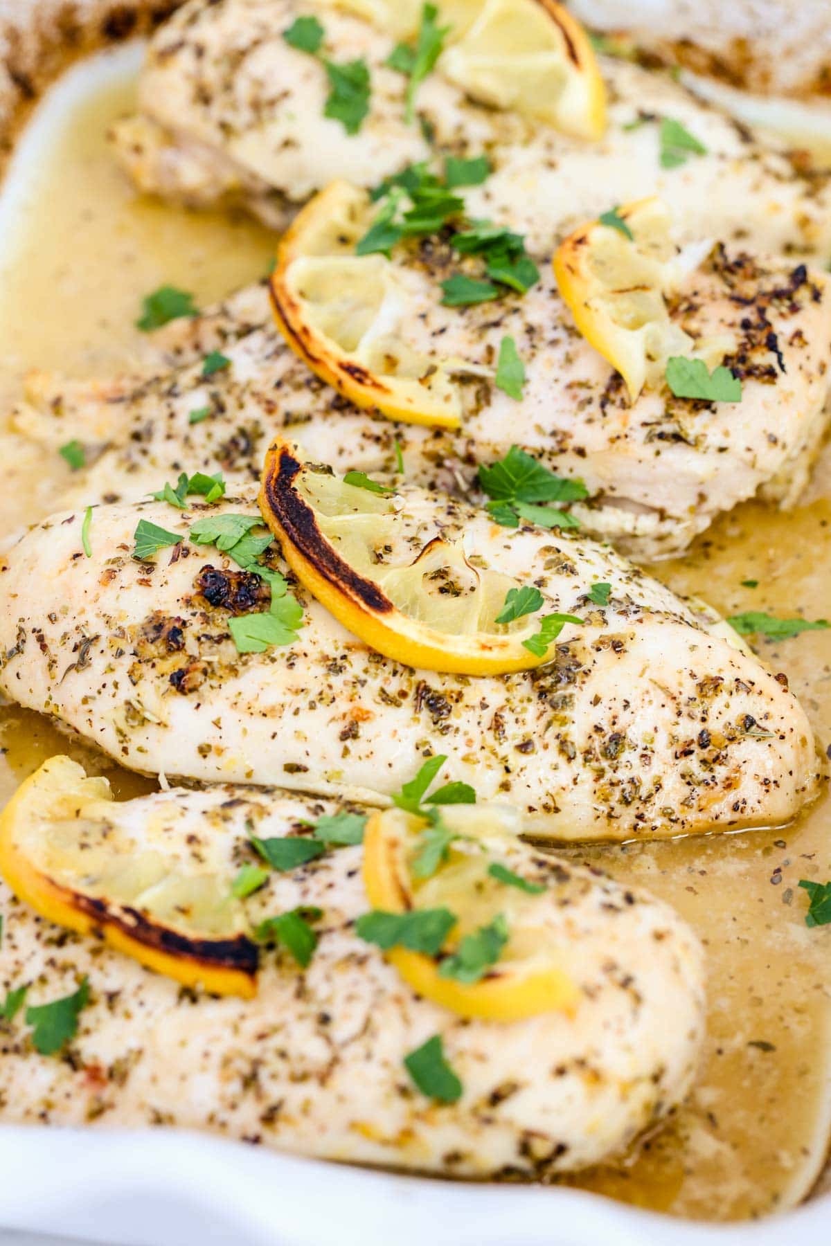 4 cooked chicken breasts with lemon slices and minced parsley.