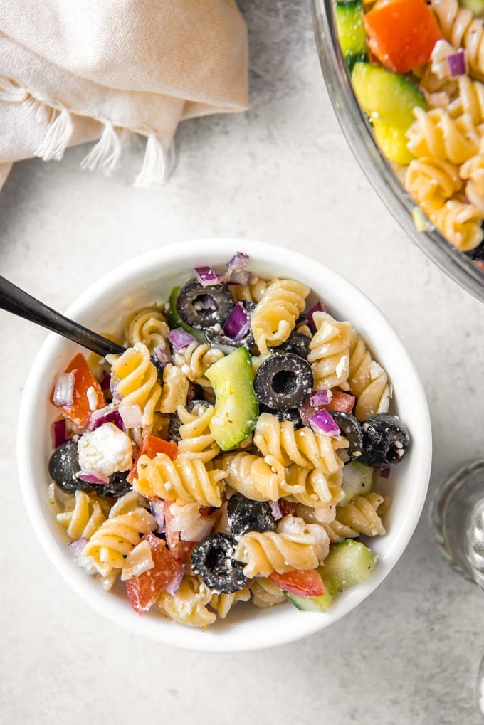 A bowl of greek pasta salad with a spoon.