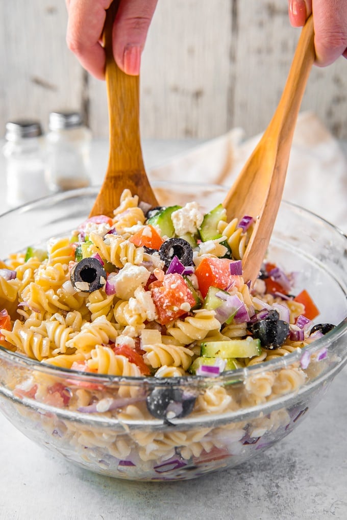 Greek pasta salad in a large bowl being tossed with salad tongs.